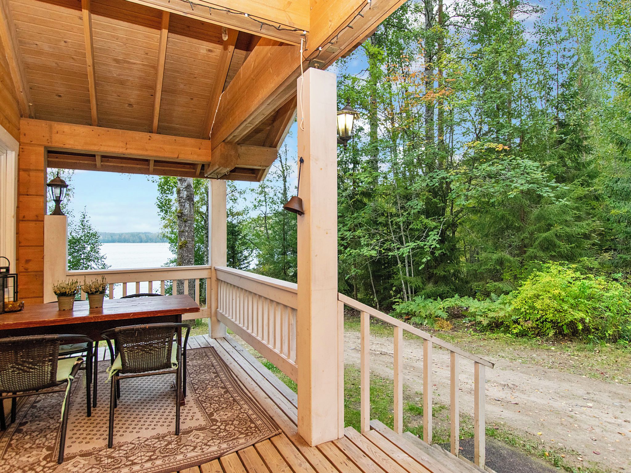 A wooden deck with a table and chairs, overlooking a lake and surrounded by trees.