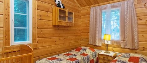 A cabin with two beds, a wooden crib, a window, and a cabinet with a stuffed panda.