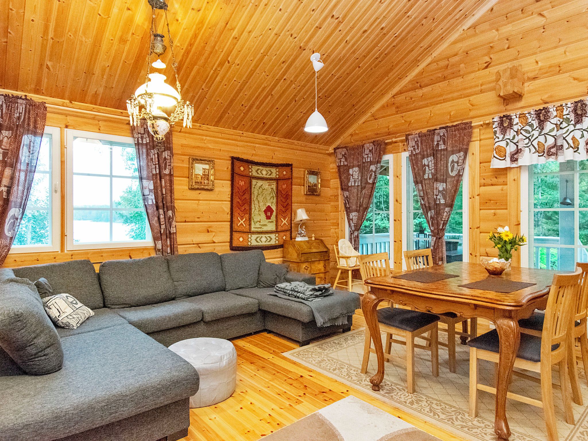Interior acogedor de una cabaña de troncos con un sofá seccional, una mesa de comedor con sillas y una araña.