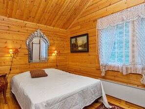 Habitación de cabaña de madera con una cama, un espejo, un cuadro y dos lámparas fijadas a la pared.