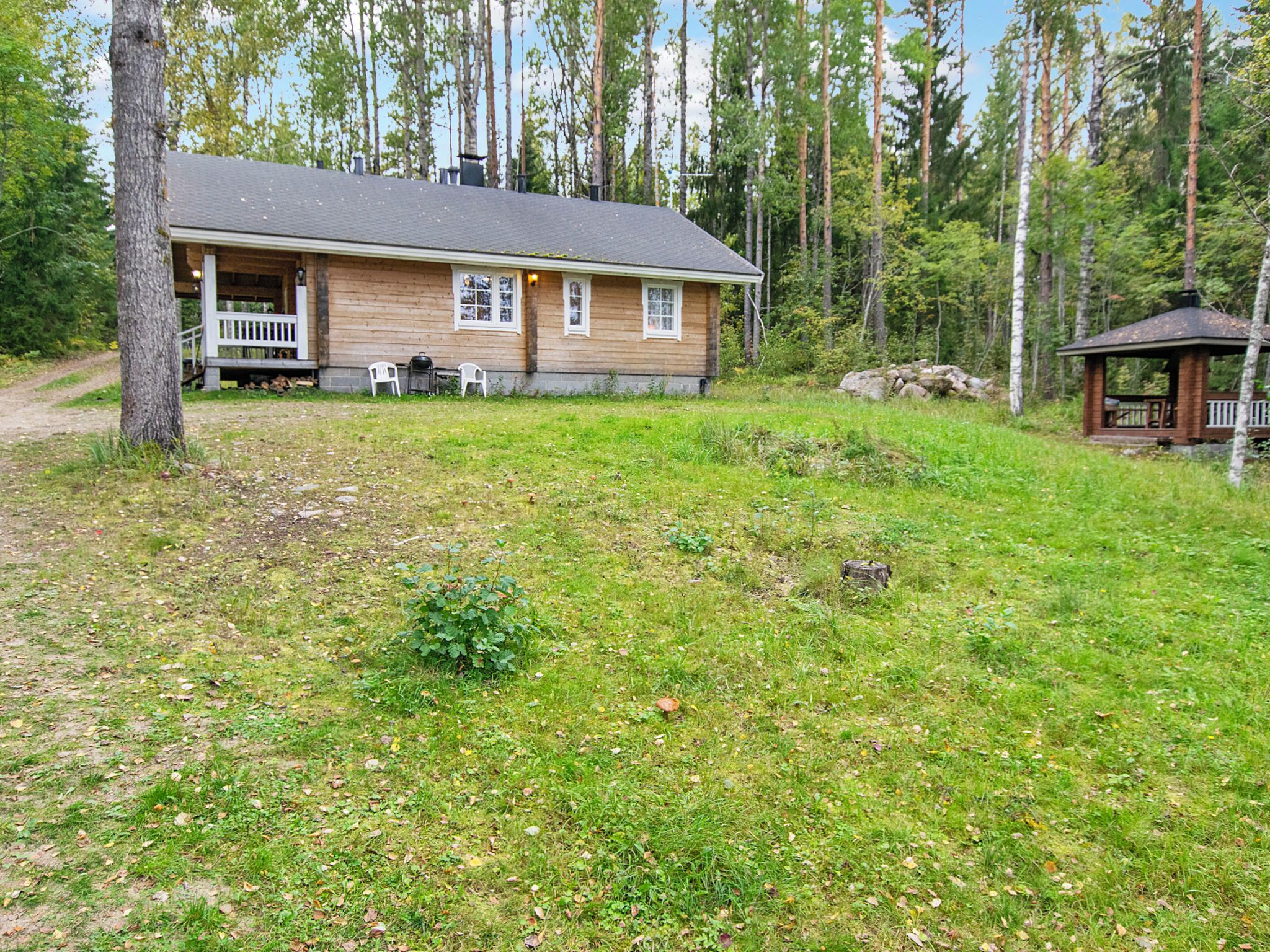 A wooden cabin with a porch, a small deck, and a shed in a forested area.
