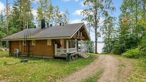 Une cabane en bois avec un porche, une cheminée et une vue sur un lac.
