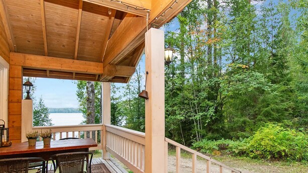 Une terrasse en bois avec une table et des chaises, donnant sur une zone boisée et un plan d’eau.