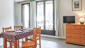 A dining area with a table set for four, wooden chairs, a television on a dresser, and a window with curtains. - Gentiane by Interhome (Chamonix)