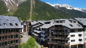 A mountain resort with multi-story buildings, balconies, and a clear view of snow-capped mountains in the background. - Gentiane by Interhome (Chamonix)