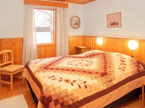 A cozy bedroom with a wooden headboard, a quilted bedspread, a bedside table, and a window with curtains. - Pesäkolo by Interhome (Kuusamo)