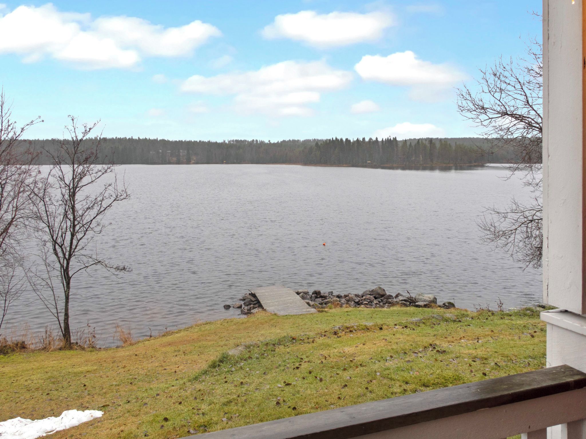 A view of a lake with a dock extending into the water, surrounded by trees and a grassy area.