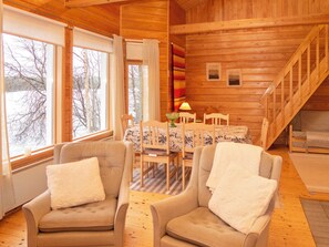 A cozy cabin interior with a dining area, two armchairs, a table with a lamp, and a staircase. - Pesäkolo by Interhome (Kuusamo)