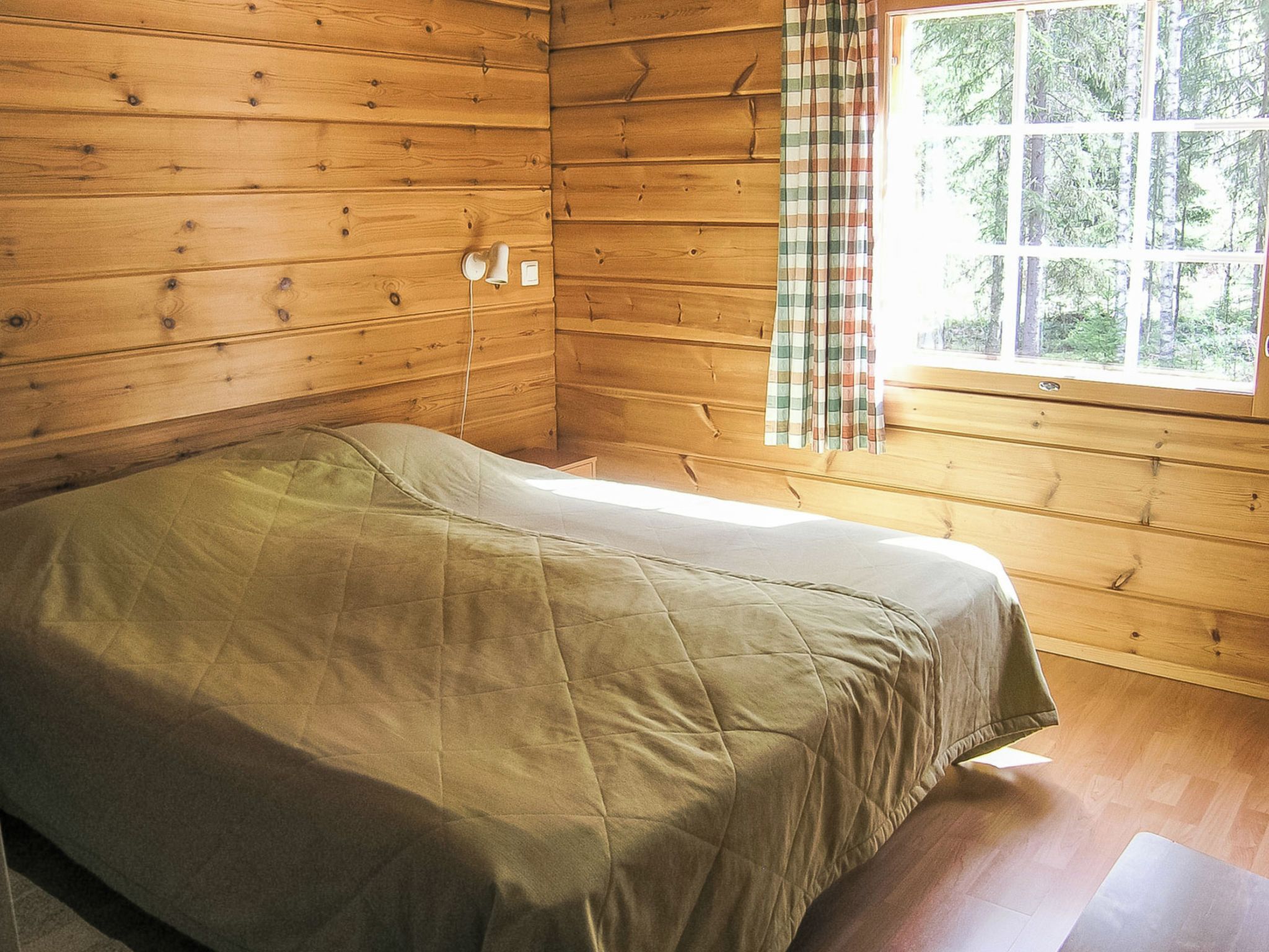 Una cama individual en una cabaña con paredes de madera y una ventana con cortinas.