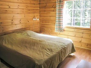 Ein Einzelbett in einer Holzhütte mit Vorhängen am Fenster.
