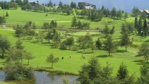 A golf course with a pond, trees, and buildings in the background.