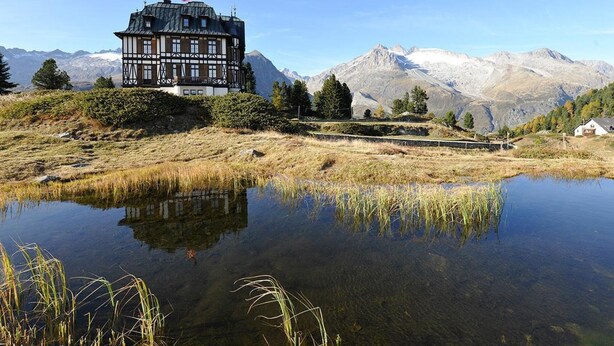 A traditional chalet with a view of mountains and a lake.