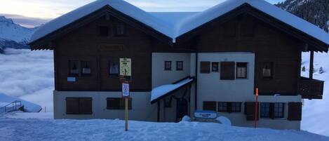 Un edificio de madera de dos pisos con techo cubierto de nieve, un letrero que indica restaurante y un cartel de alquiler de esquíes.