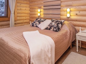 A cozy log cabin bedroom with a bed, pillows, a bedside table, and wall-mounted lights.