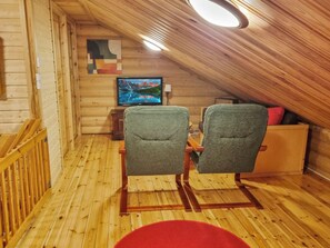A cozy cabin with a wooden interior, a television mounted on the wall, and two chairs facing a small table.