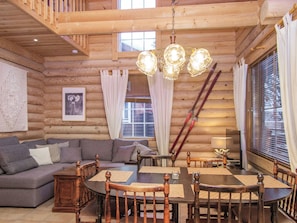 A log cabin interior with a dining table, chairs, a sofa, and a chandelier.