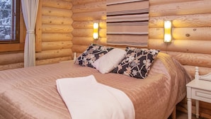 A cozy log cabin bedroom with a large bed, two wall-mounted lights, and a wooden headboard. - Tahkon tikka by Interhome (Nilsiä)