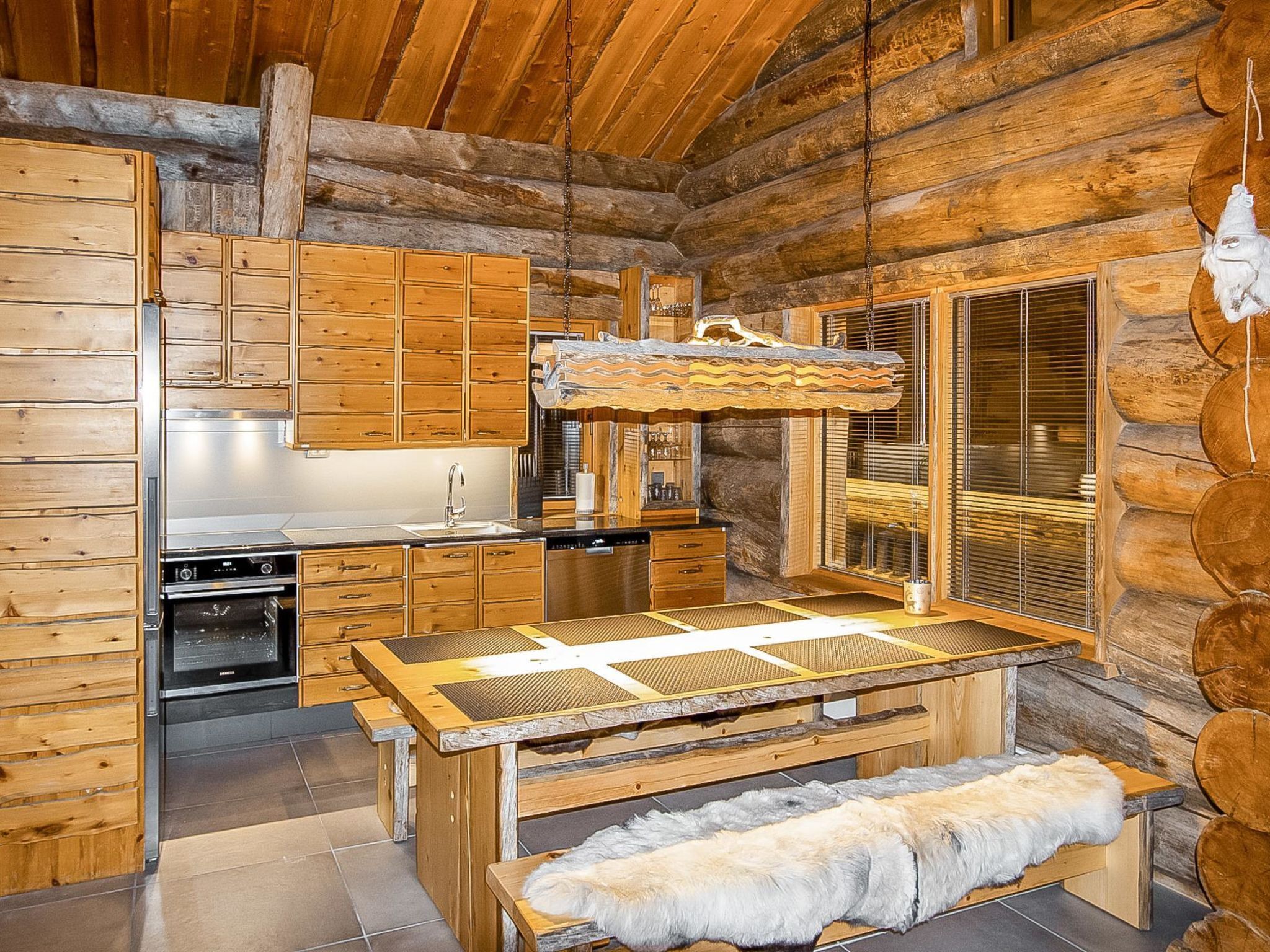 Interior de una cabaña de troncos con armarios de madera, una chimenea de piedra y una mesa con bancos.