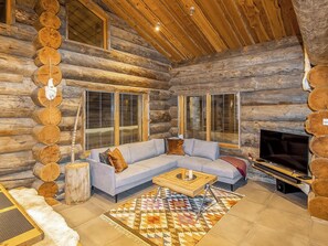 A log cabin interior with a sectional sofa, a television, and a patterned rug.
