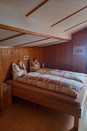 Ein Einzelbett mit Patchworkdecke, Holz-Kopfbrett und einem kleinen Nachttisch.