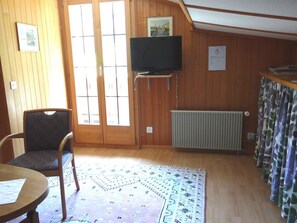 Ein Zimmer mit Holzwänden, einem Fernseher auf einem Schrank, einem Sessel, einem Tisch und einem gemusterten Teppich.