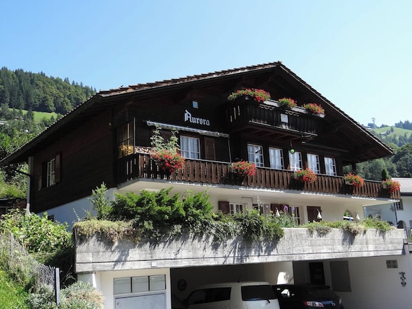 A two-story wooden building with balconies, a sign reading 'Aurora,' and a parking area in front.