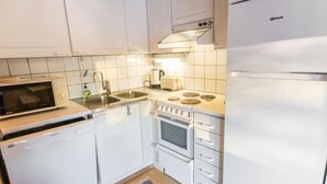 A compact kitchen with white cabinets, a microwave, a sink, a stove, and a refrigerator. - Tunturinvieri k3 by Interhome (Ylläsjärvi)