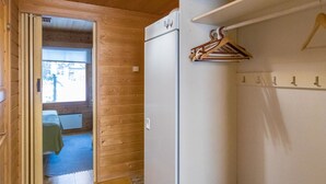 A compact room with a wooden interior, a white refrigerator, a small seating area with a table, and a hanging clothes rack. - Tunturinvieri k3 by Interhome (Ylläsjärvi)
