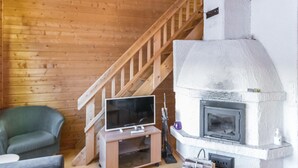 A cozy living room with a wooden staircase, a fireplace, a television on a wooden stand, and a green armchair. - Tunturinvieri k3 by Interhome (Ylläsjärvi)