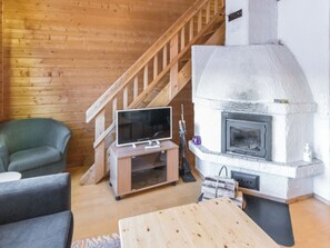 A cozy living room with a wooden staircase, a television on a stand, and a stone fireplace.