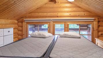 A log cabin bedroom with two beds, a window, and a ceiling light.