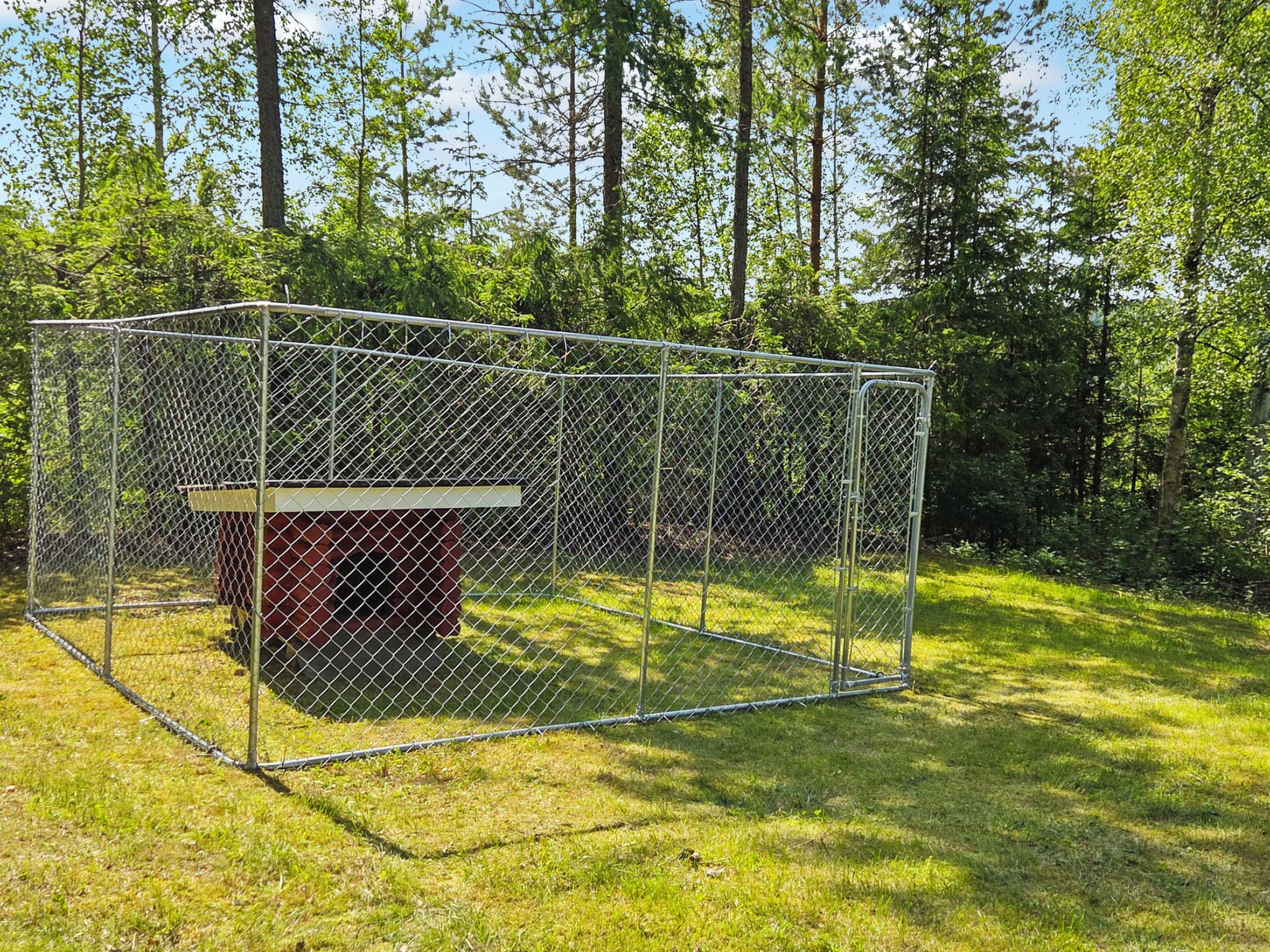 A fenced enclosure with a bench and a small structure, surrounded by grass and trees.