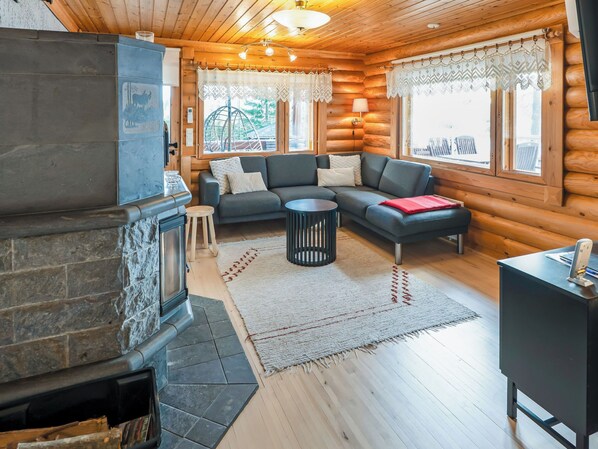 Ein Blockhaus-Interieur mit Kamin aus Stein, einem grauen Sofa und einem kleinen runden Tisch.