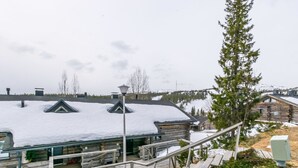 Une cabane en rondins dont le toit est recouvert de neige, avec un escalier en bois menant à l’entrée, et une vue sur la forêt environnante.