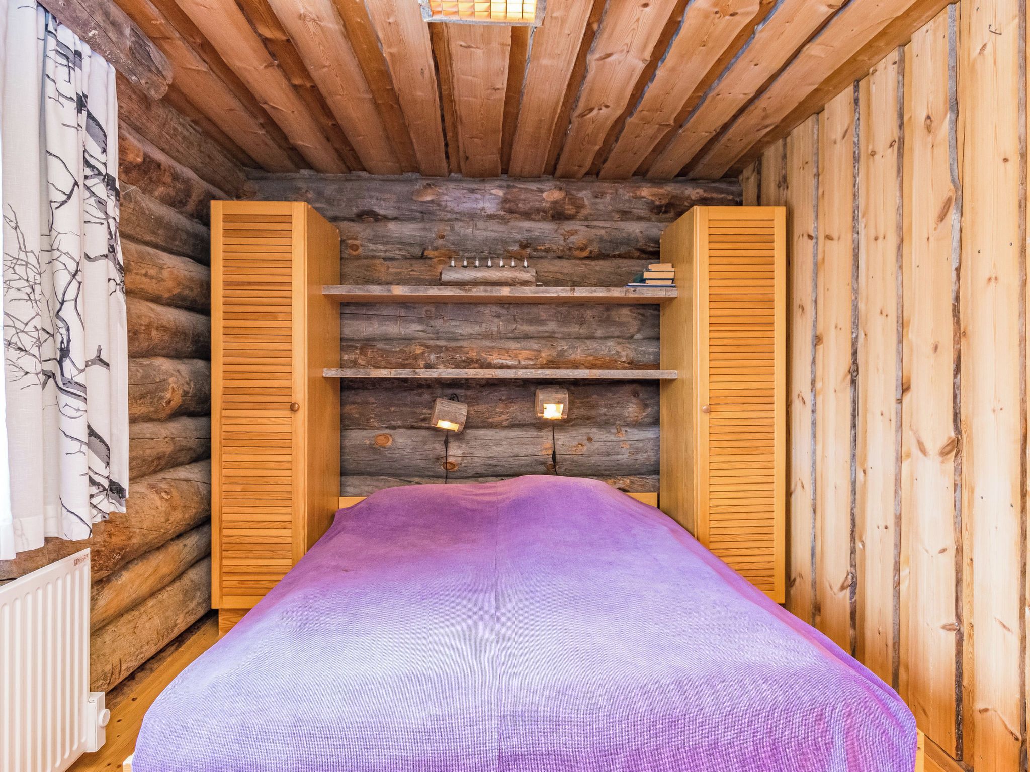 Une chambre aménagée dans un chalet en rondins, avec un lit, des étagères en bois et une fenêtre.