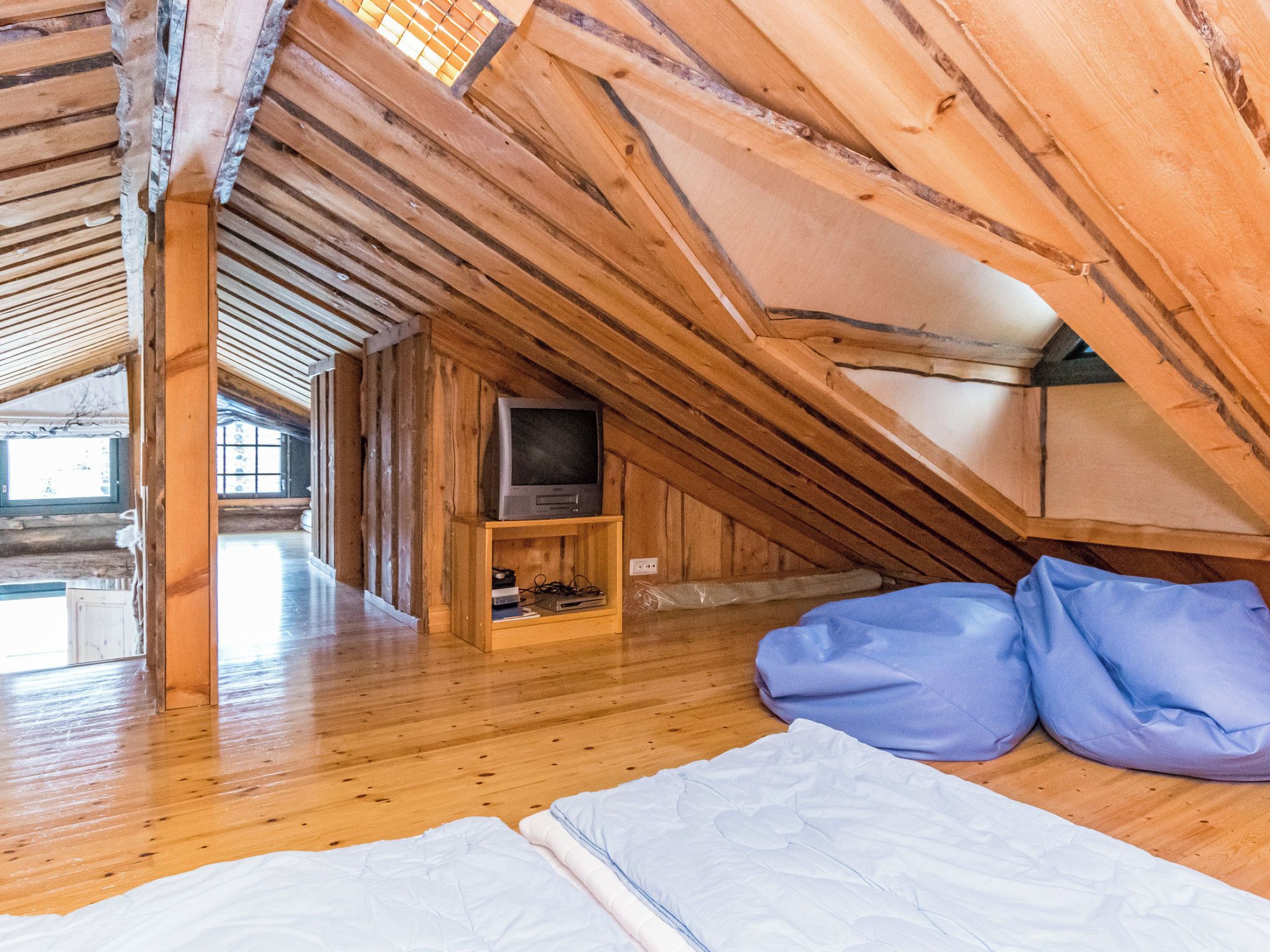 Une chambre mansardée en bois, avec un plafond en pente, un téléviseur posé sur une étagère et un lit avec des oreillers.