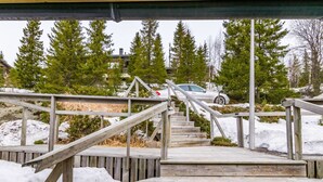 Un escalier en bois mène à une zone abritée, délimitée par des rampes de métal, et entourée de neige et d’arbres.
