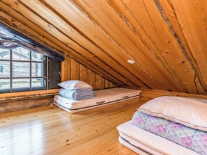 A small attic bedroom with wooden walls, a window, and a mattress.