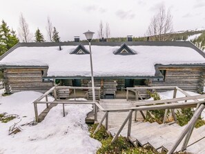 A log cabin with a snow-covered roof and a wooden deck leading to the entrance.