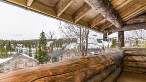 Une cabane en rondins dotée d’une terrasse en bois et offrant une vue sur un paysage enneigé, avec des bâtiments visibles au loin.