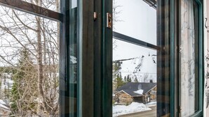 Une fenêtre donnant sur un paysage enneigé, avec notamment un chalet et un télésiège.