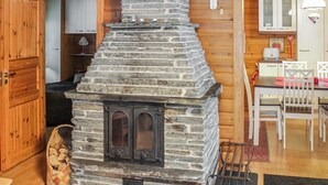 Una chimenea de piedra con chimenea, una mesa de comedor de madera con sillas, y una zona de cocina con armarios y una lámpara colgante.