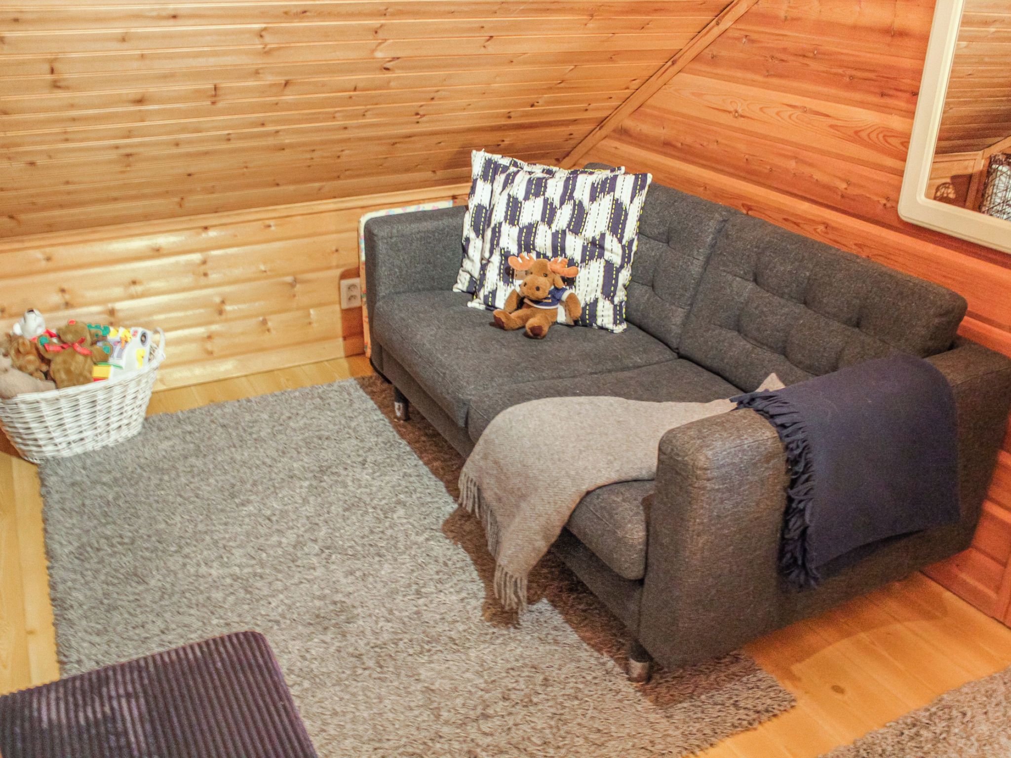 A cozy room with a grey sofa, a patterned pillow, a small basket of items, and a grey rug.