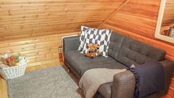 A cozy room with a grey sofa, a patterned pillow, a small basket of items, and a grey rug.