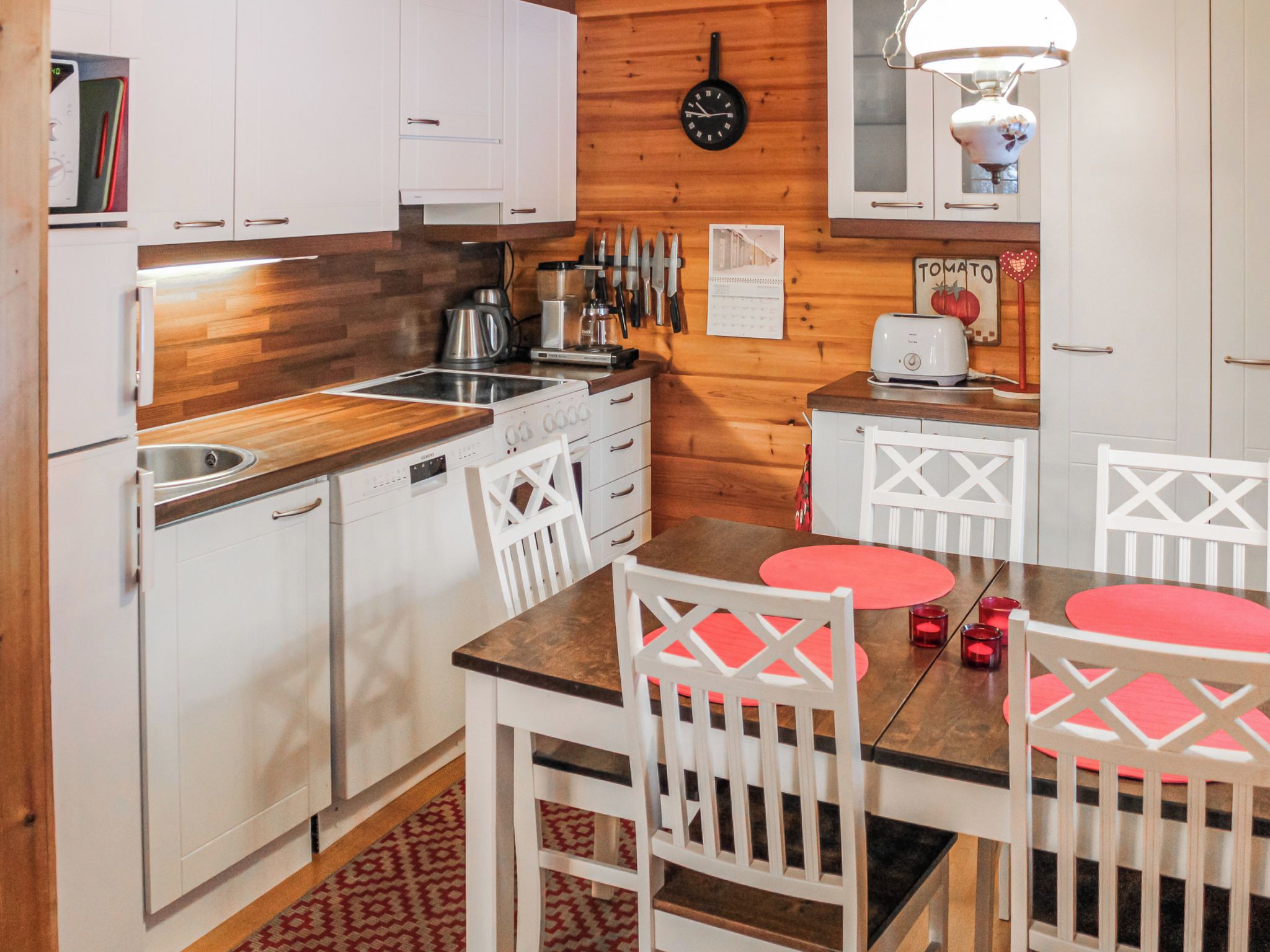 A compact kitchen with white cabinetry, a wooden countertop, a stove, and a dining area with white chairs and red placemats.