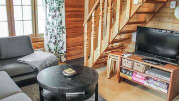 A cozy living room with a sofa, a coffee table, a TV stand with a flat-screen TV, and a staircase.