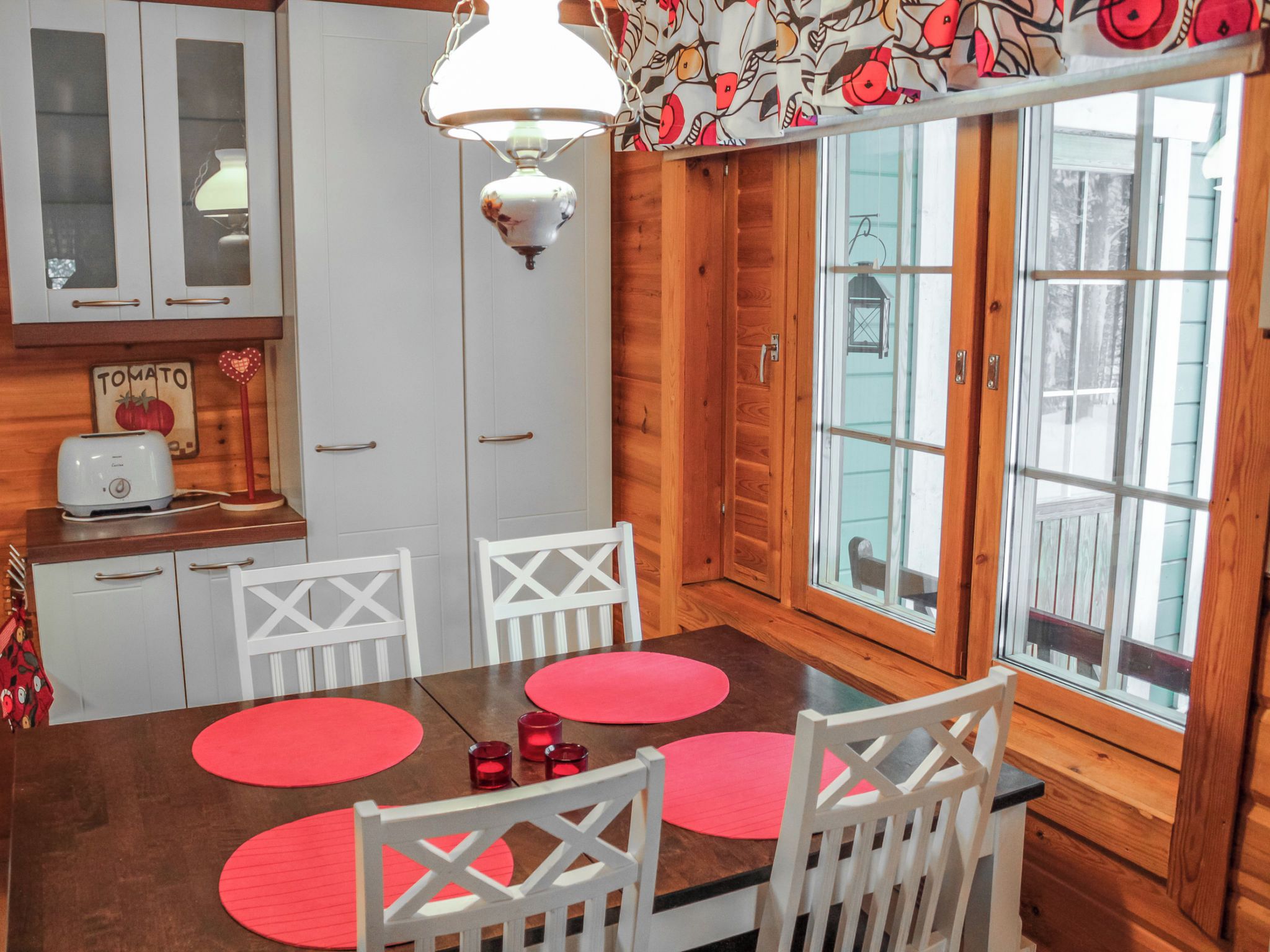 A kitchen with white cabinets, a wooden table with red placemats, and a hanging light fixture.