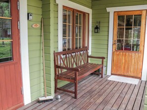 En träbänk på en veranda med en grön dörr och fönster.