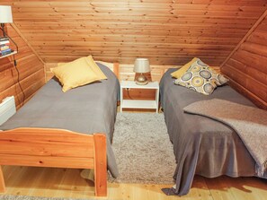 Una habitación pequeña y acogedora con dos camas individuales, una mesita de noche con lámpara y un cabecero de madera.