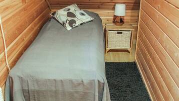 A small, cozy room with a single bed, a bedside table with a lamp, and a small wicker basket.